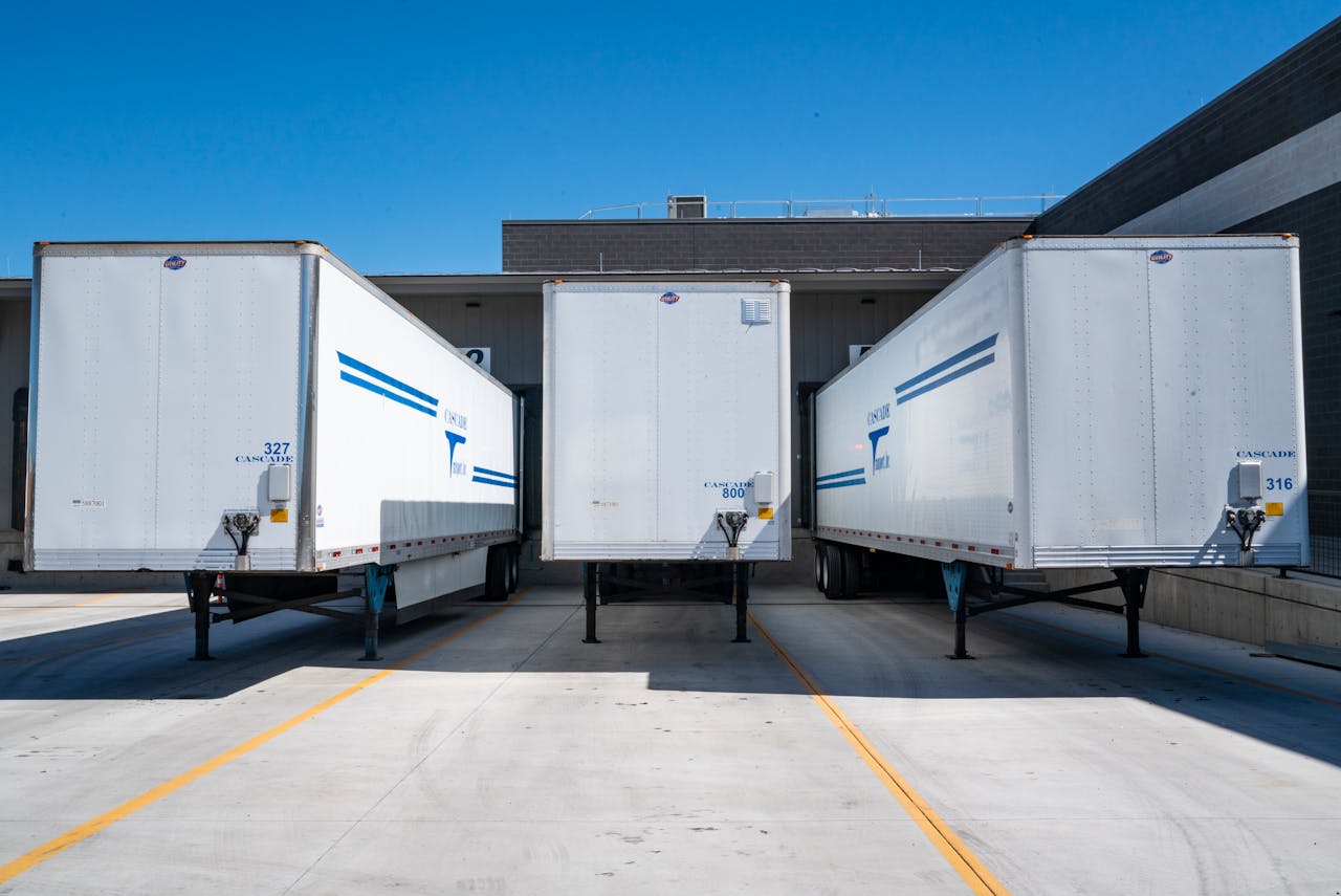 services-02 Three white cargo trailers parked at an industrial shipping dock under clear blue skies.